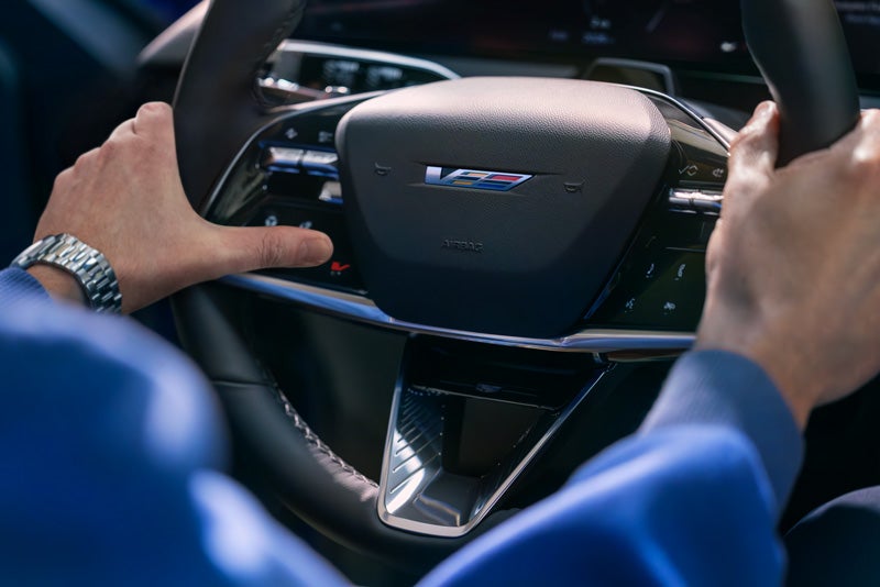Close-up of a Man About to Press the V-Button on the 2026 OPTIQ-V Steering Wheel | Schwan Cadillac in Mandan ND