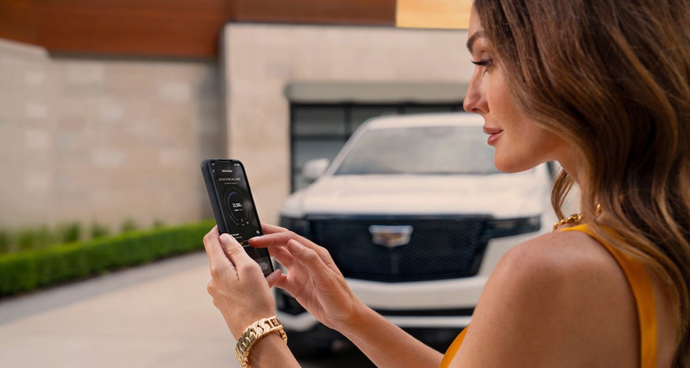 lady checking her mobile with a Cadillac vehicle background | Schwan Cadillac in Mandan ND